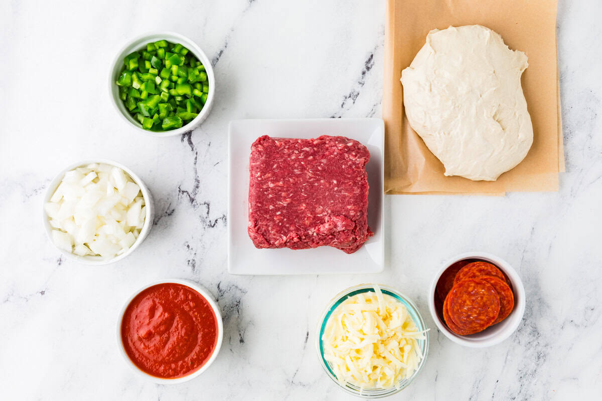 Ingredients for meaty cast iron calzone lined up on a white counter.