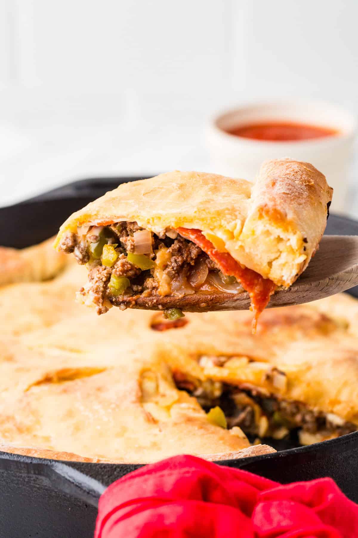 Slice of a meaty calzone being lifted from a pan on a wooden spoon.