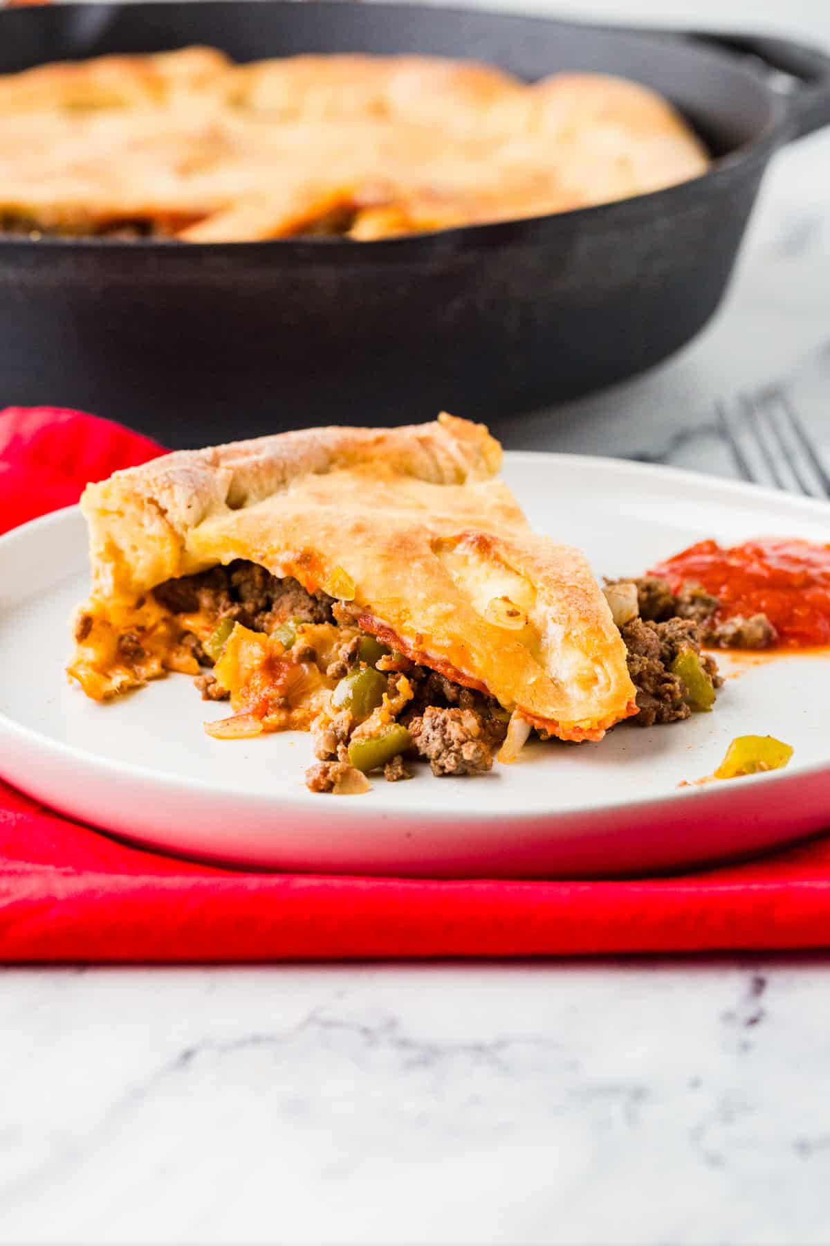 Slice of a meaty calzone on a white plate, next to a cast iron pan.