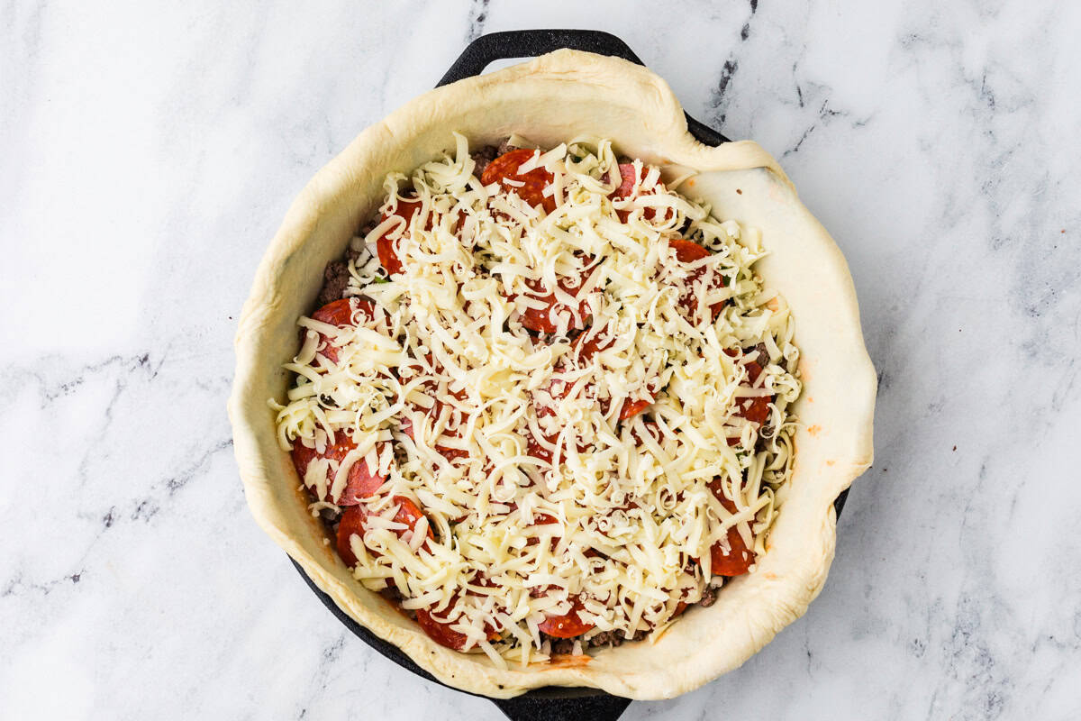 Dough hanging over the edges of a cast iron pan with filling ingredients inside.