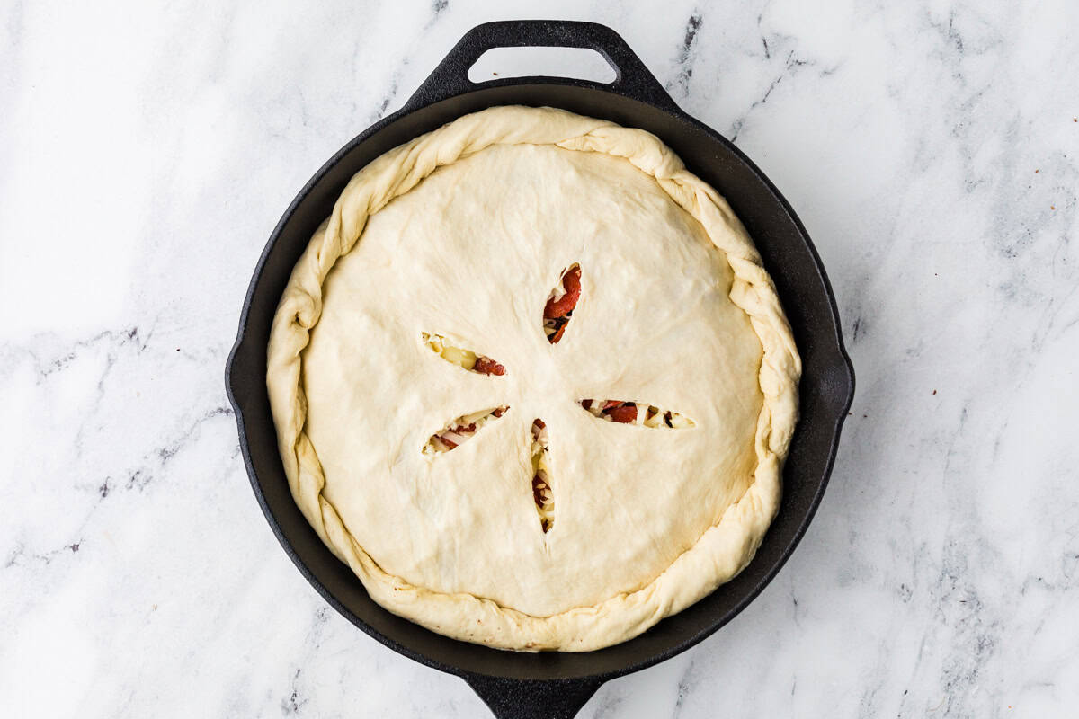 Calzone in a pan before baking, with dough over the top.