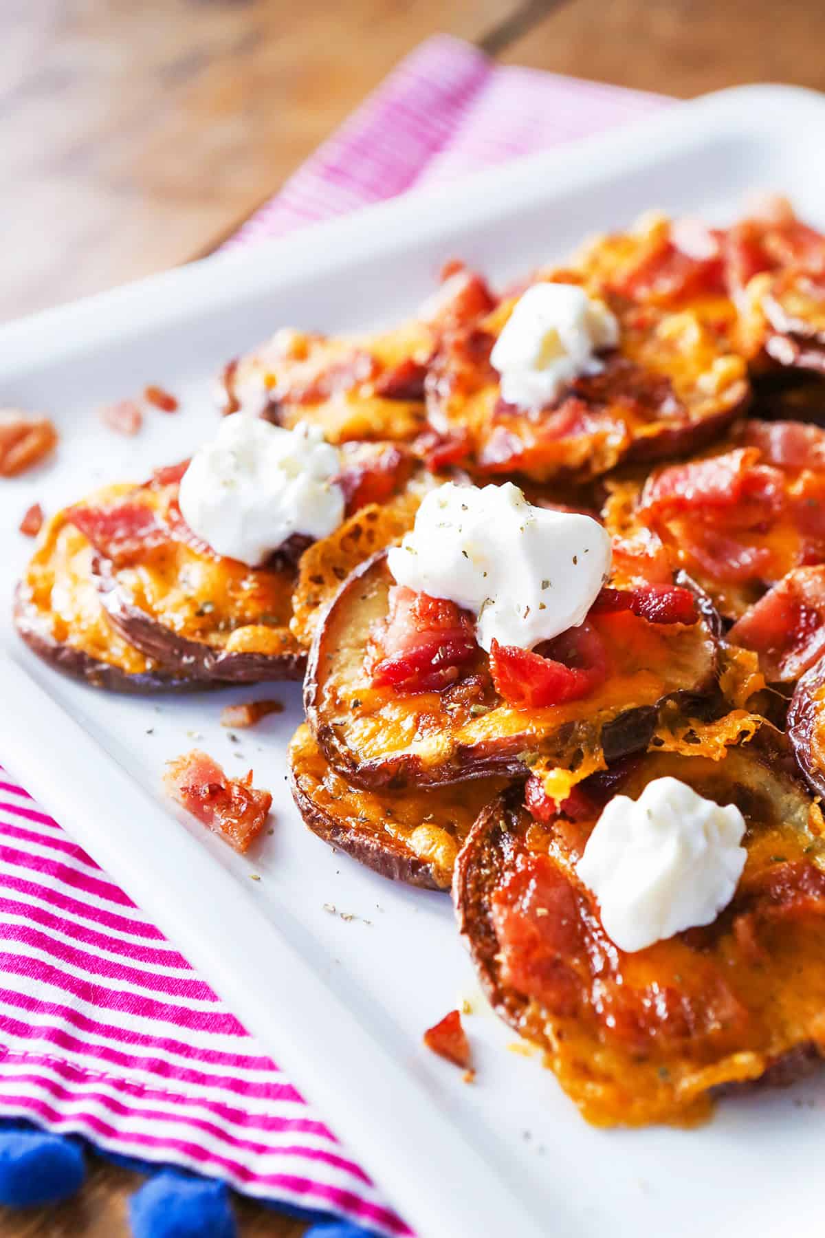 Stack of loaded potato rounds on a plate, each topped with a dollop of sour cream.