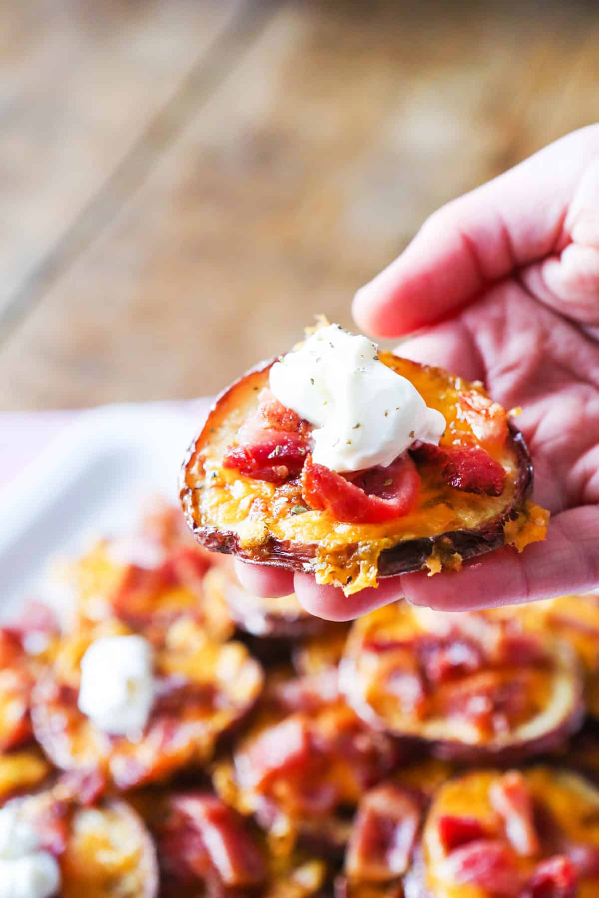 A hand holding a loaded potato round over a plate with many of them.