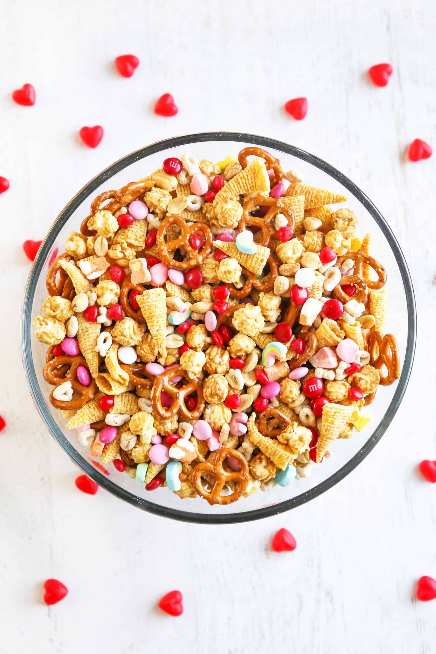 Large glass mixing bowl filled with festive valentine's day trail mix, surrounded by candy hearts.