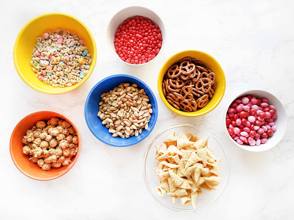 Ingredients for a valentine snack mix in individual bowls, sitting on a white counter.
