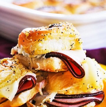 Close-up of a ham and cheese slider with melted cheese and sliced ham on Hawaiian roll.