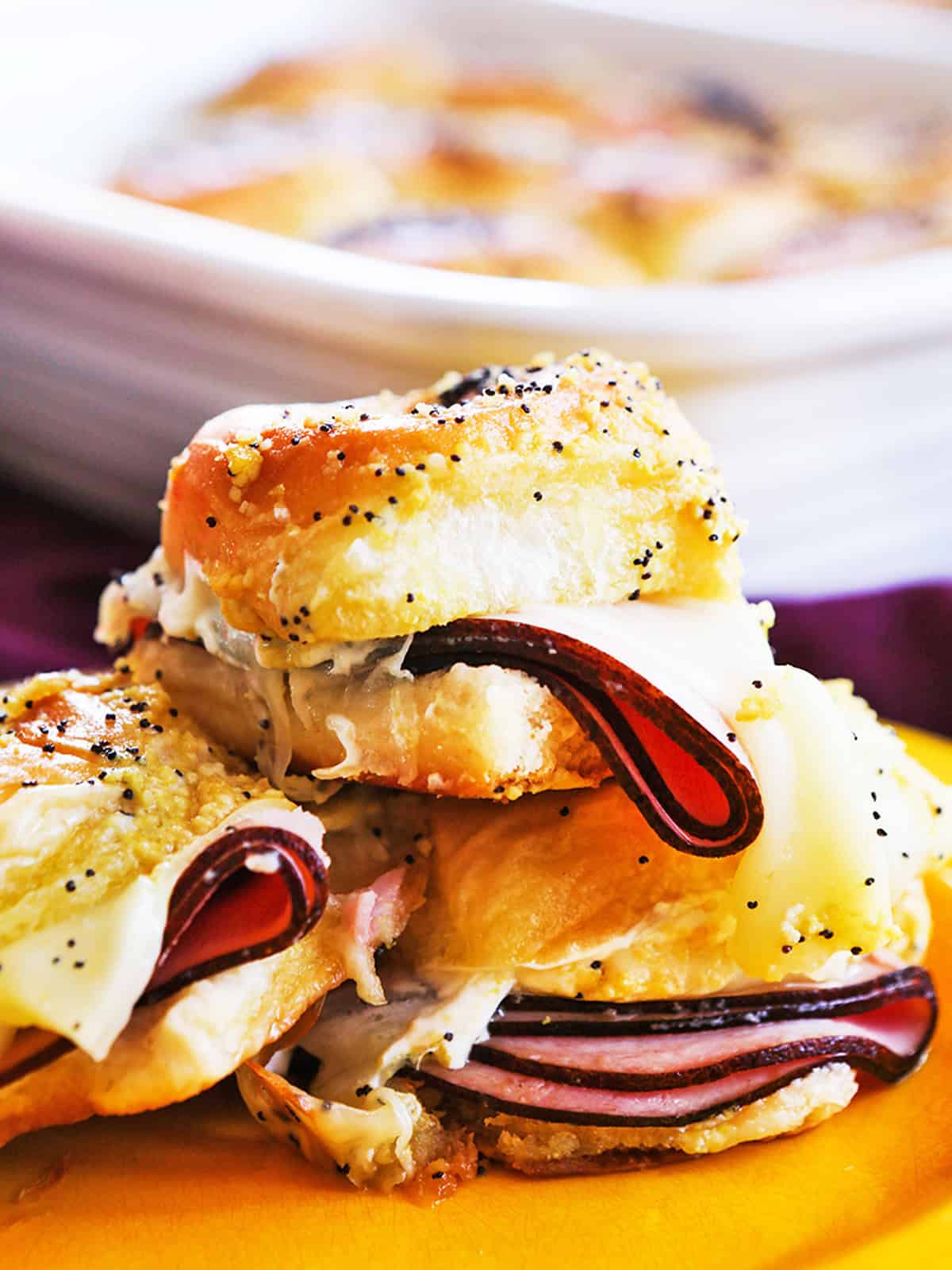 Close-up of a ham and cheese slider with melted cheese and sliced ham on Hawaiian roll.