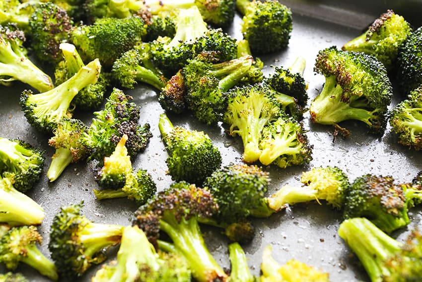 Baking sheet with roasted broccoli and seasoned with salt and pepper. 