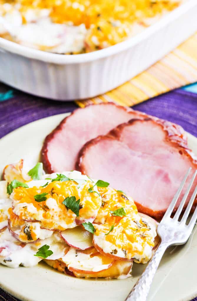 plated ham and scalloped potatoes next to a baking dish