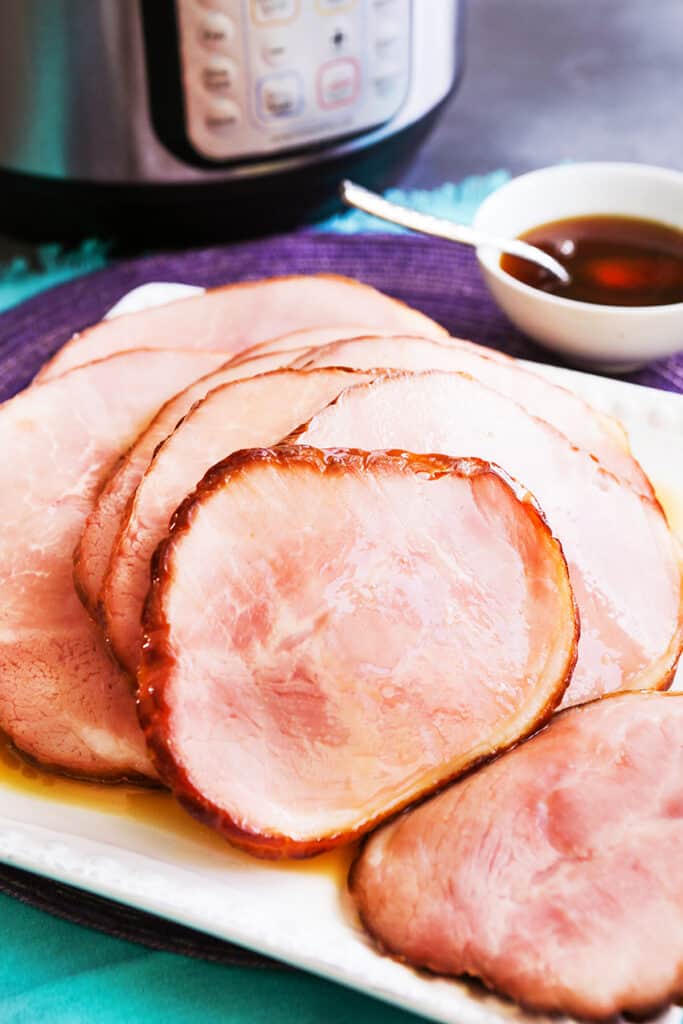 slices of ham on a serving platter, sitting next to an instant pot