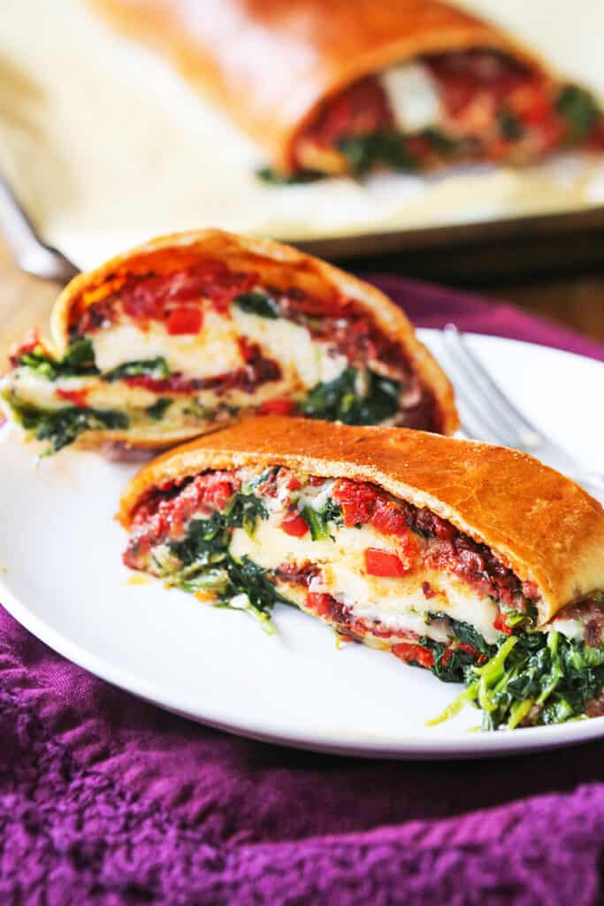 Two slices of veggie stromboli calzone on a plate with melty cheese oozing out. 