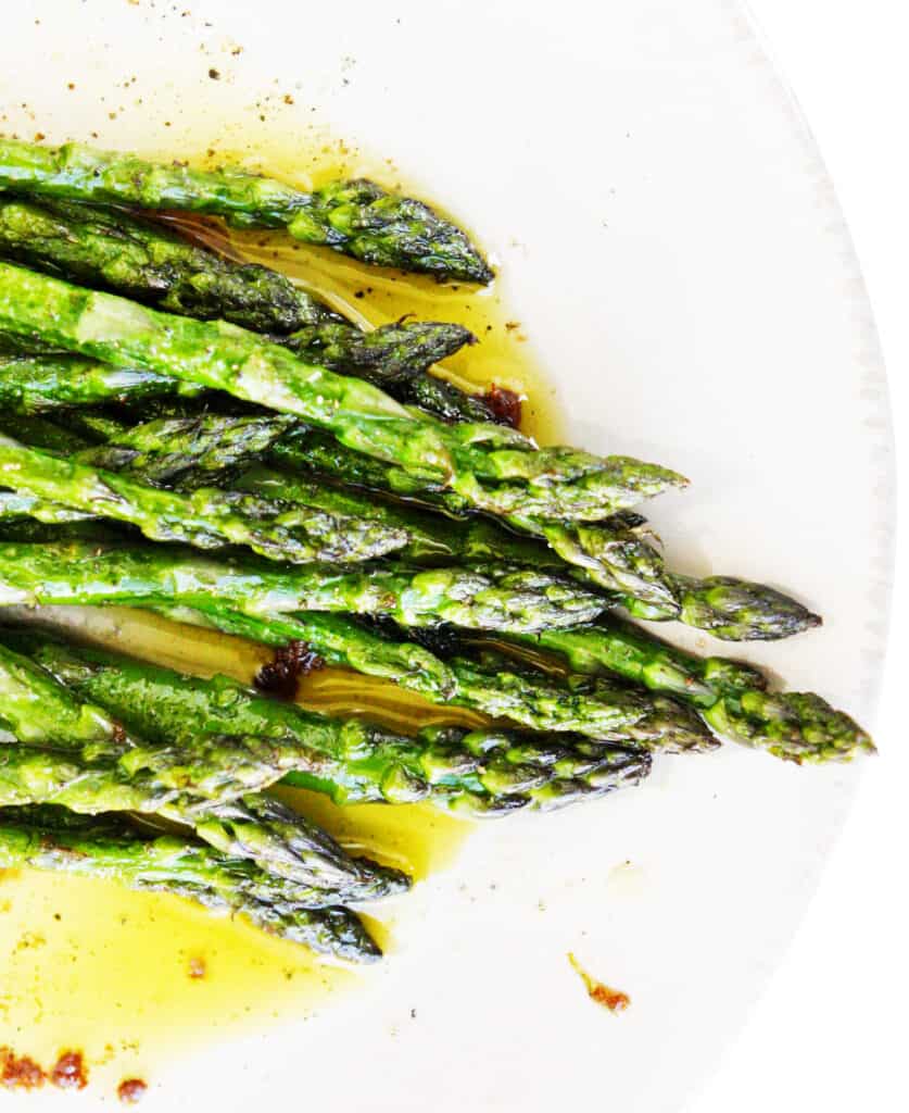 Sauteed asparagus sitting on a plate with some olive oil and spices on it. 