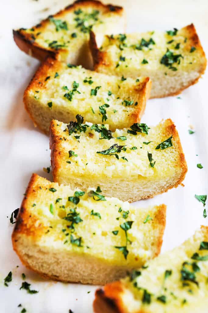 Pieces of garlic bread lined up on parchment paper.
