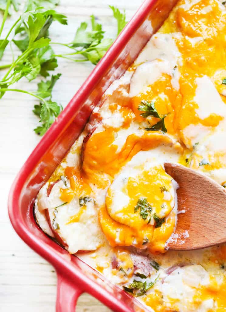 wooden spoon pulling scalloped potatoes out of a baking dish