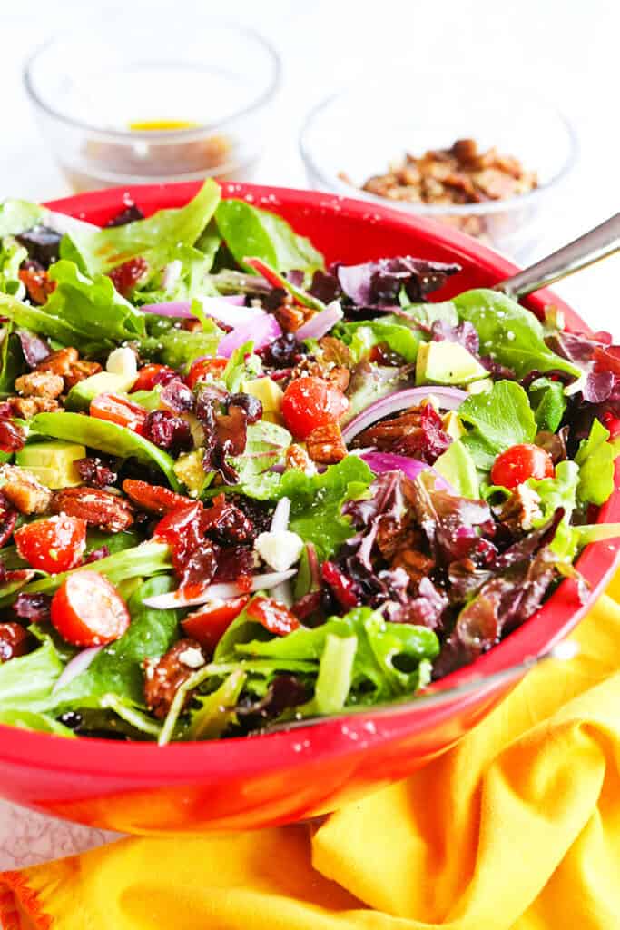 Chopped salad in a red serving bowl with a spoon tucked inside. 