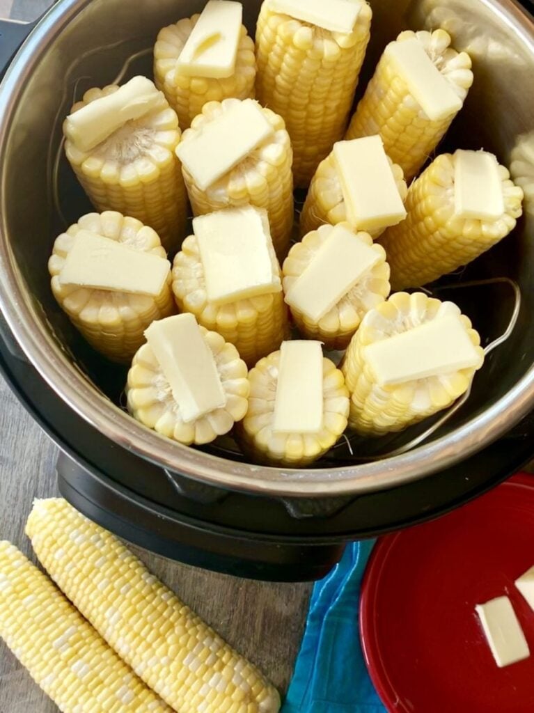 corn cobs inside the instant pot with a pat of butter on top of each one