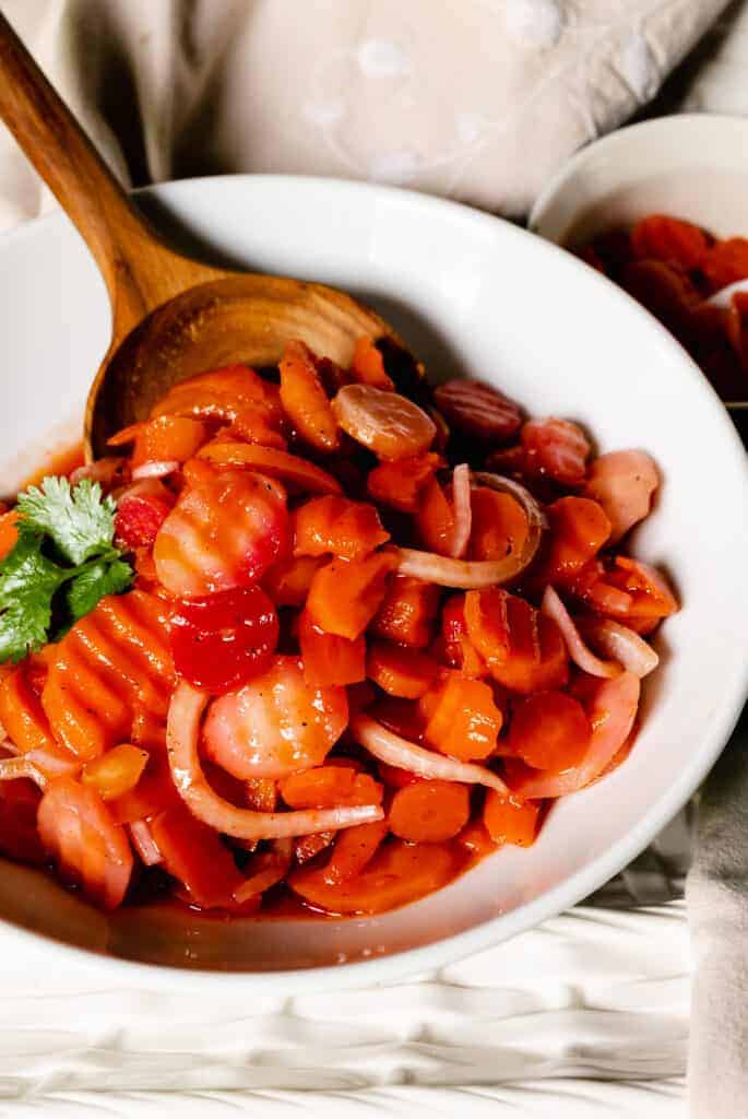 A wooden serving spoon tucked into a bowl of marinated carrot salad