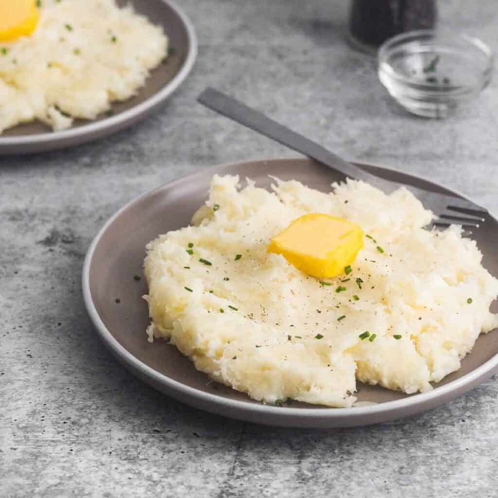 a pat of butter on top of garlic yuca mash with a fork alongside