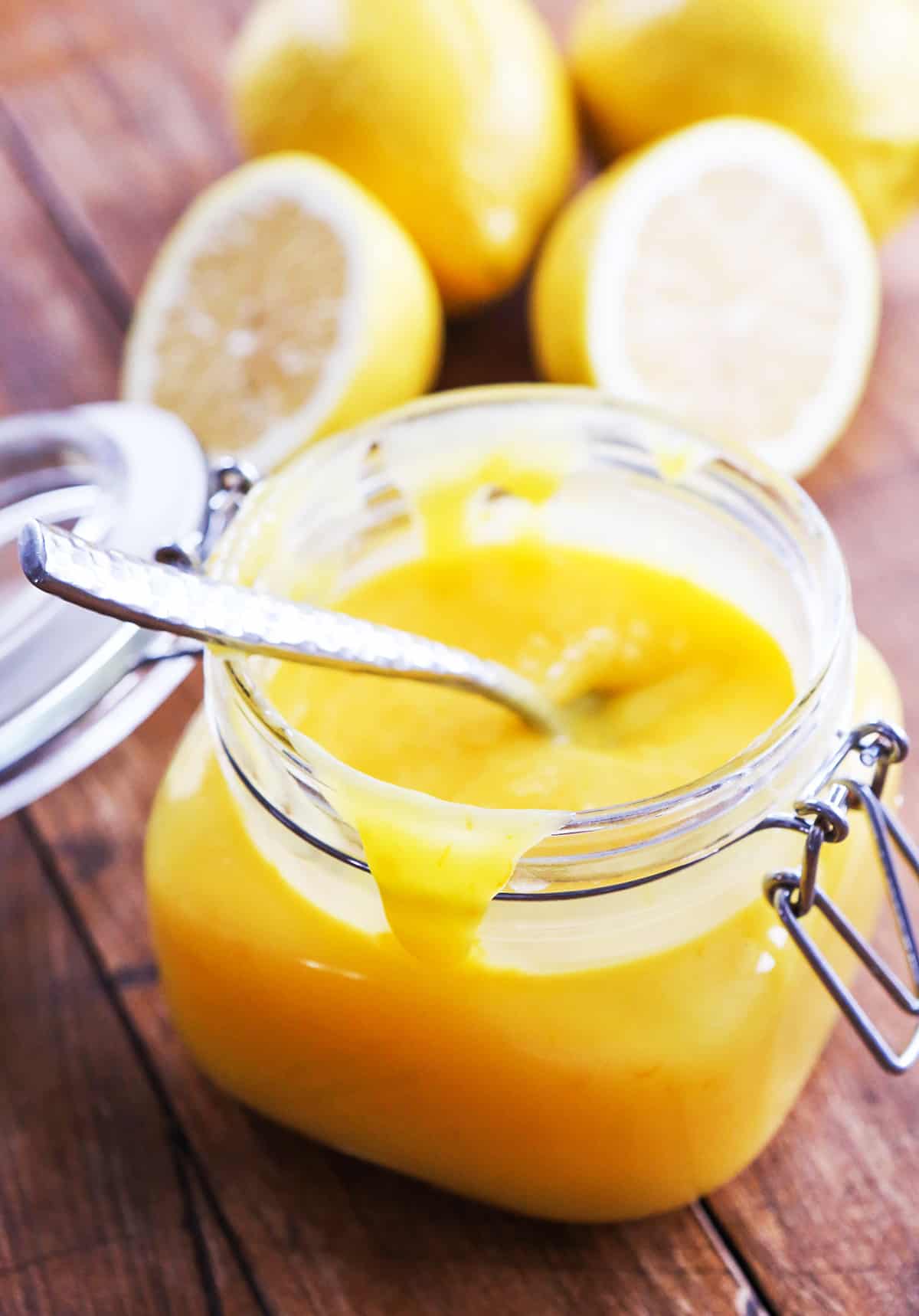 Jar filled with lemon curd, surrounded by lemons that have been cut in half.