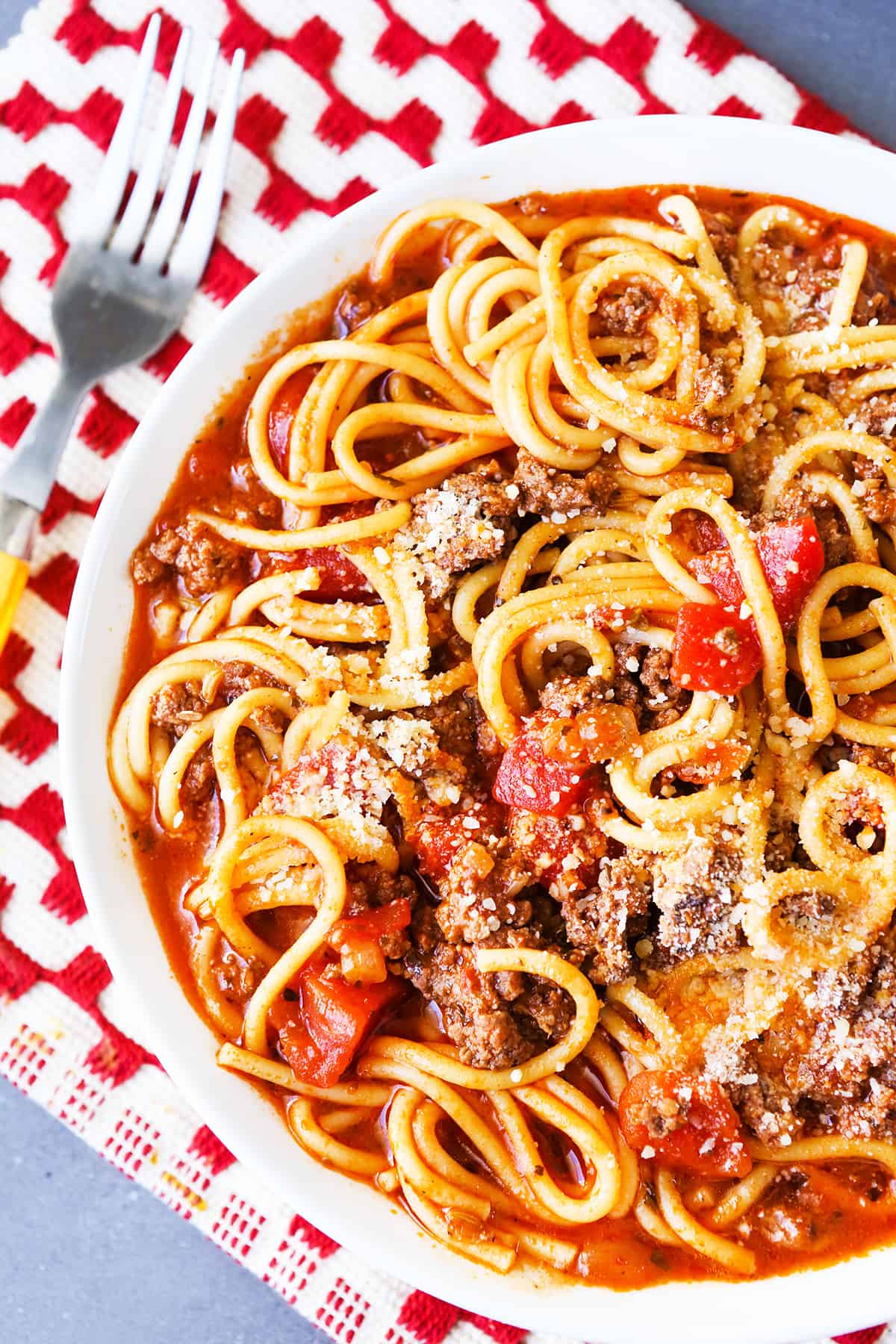 Heaping plate of spaghetti on a read and white placemat.