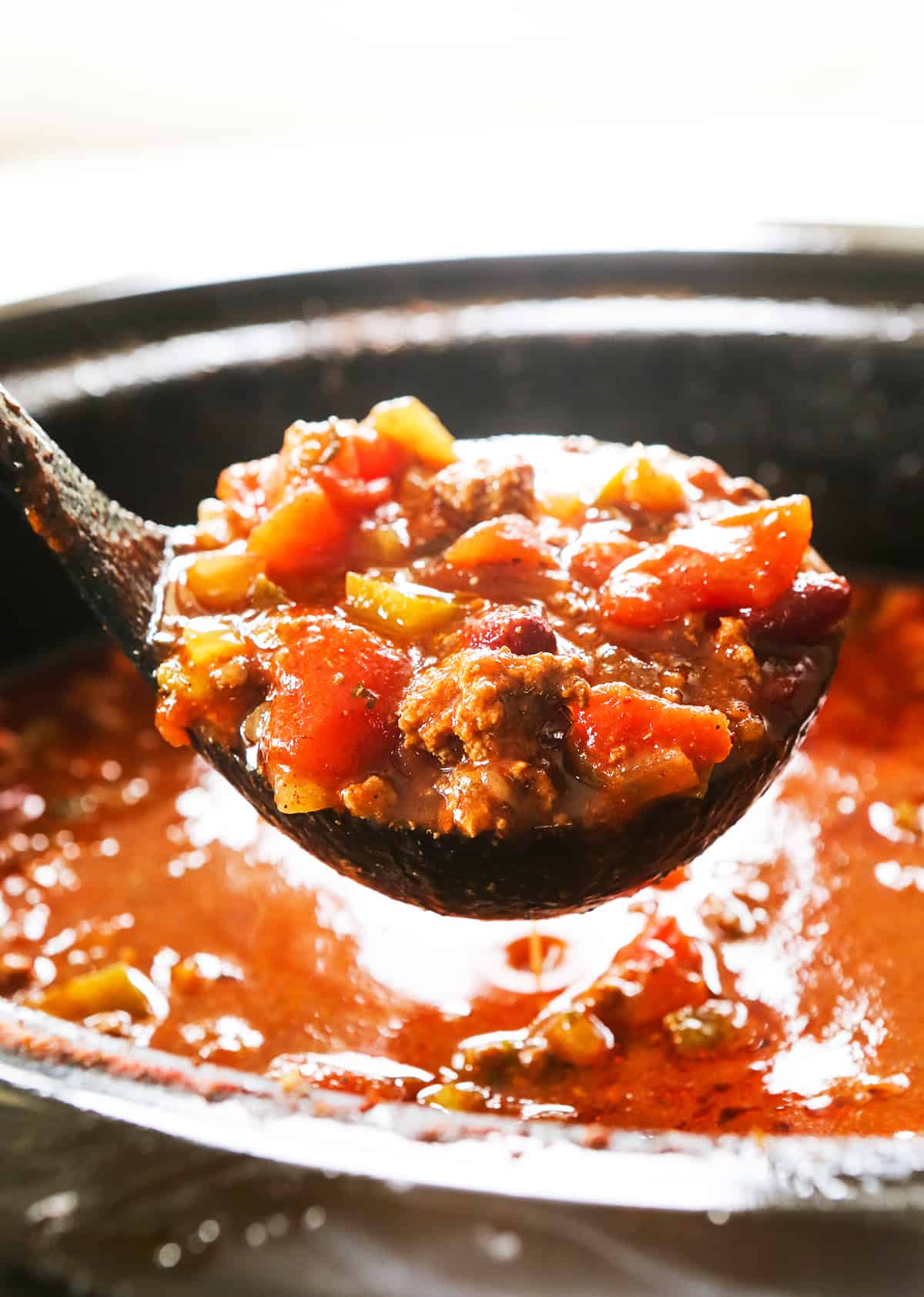 Ladle filled with chunky chili hovering over a full crockpot.