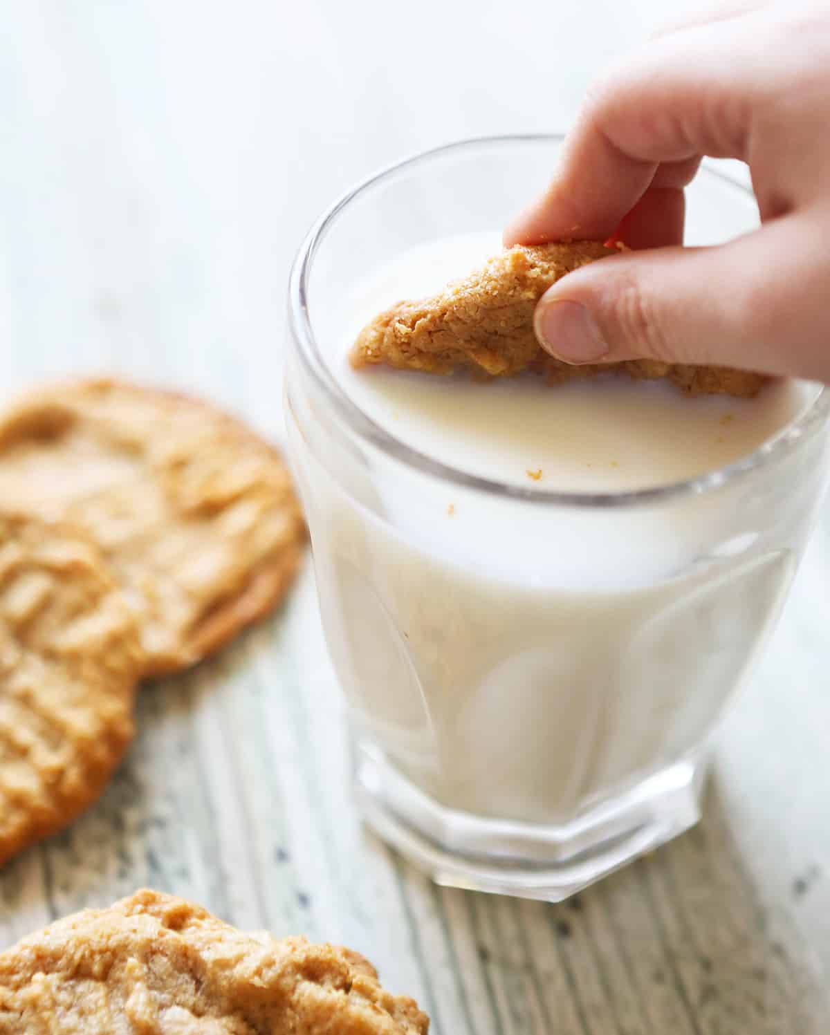 hand dunking a peanut butter cookie into a glass of milk