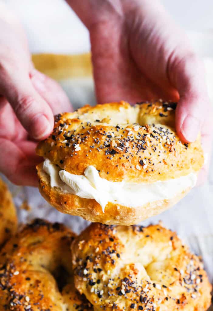 Two hands holding a bagel filled with cream cheese.