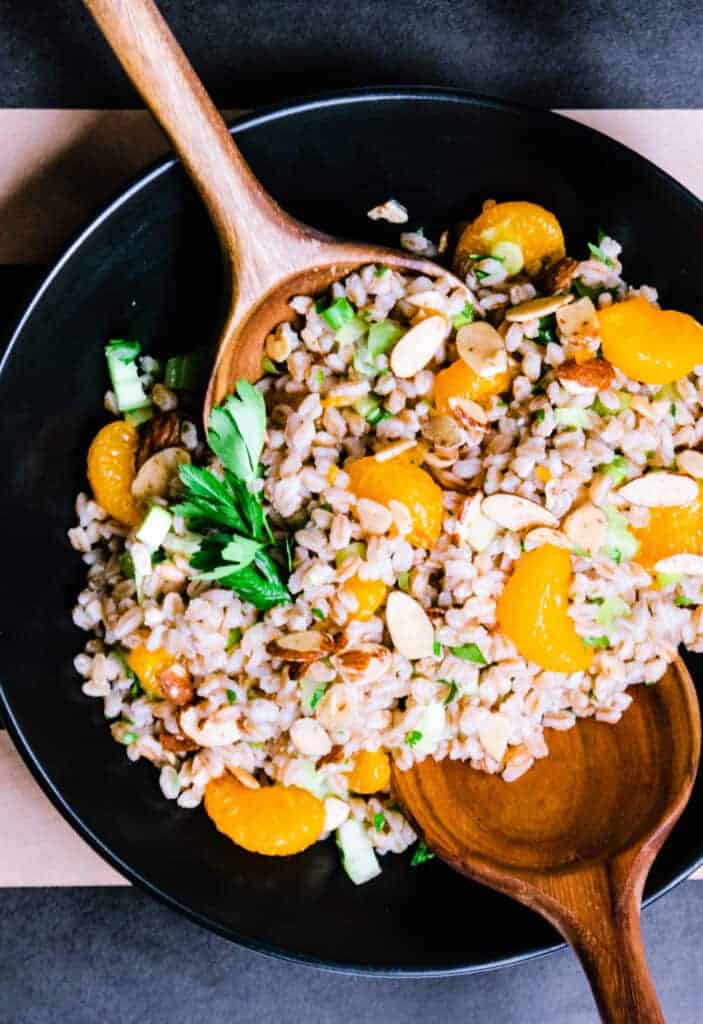 bowl of farro and orange salad with salad tongs in it