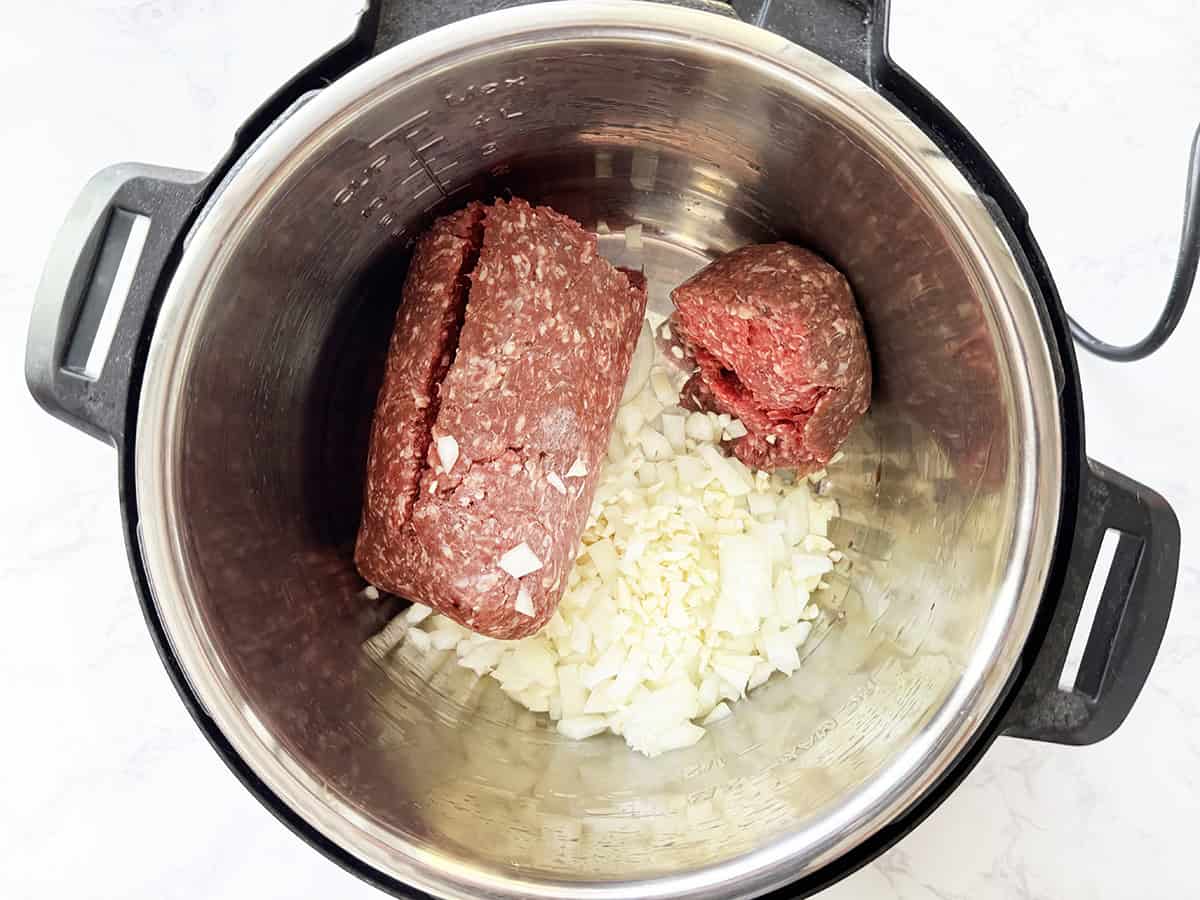 Raw ground beef, onion and garlic inside an Instant Pot.