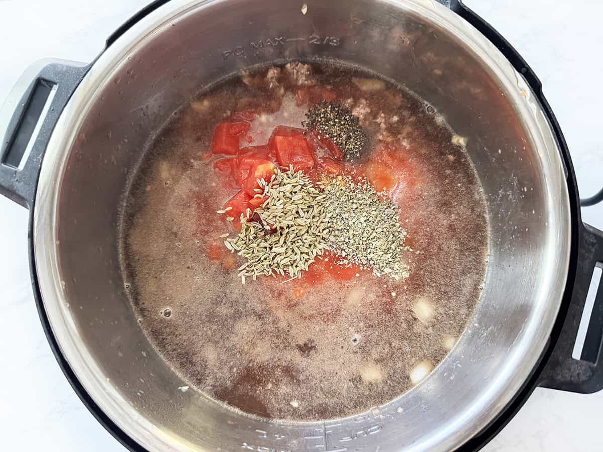 Seasonings and tomatoes mixed into the ground beef mixture in an Instant Pot.