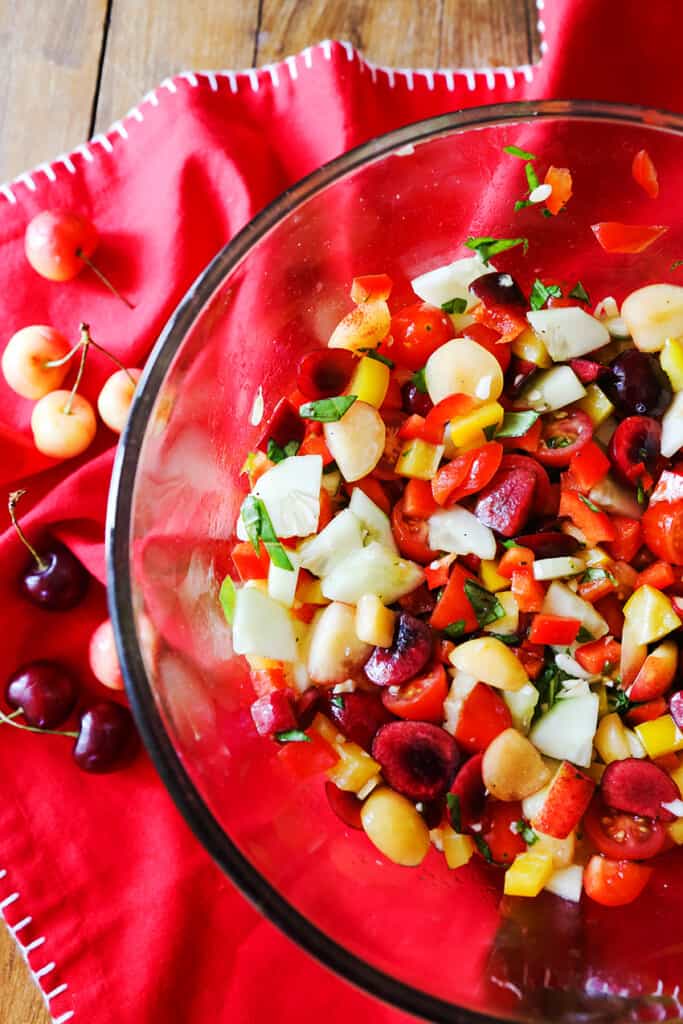 Fresh cherry gazpacho salad in a glass bowl with whole fruit scattered on the table. 