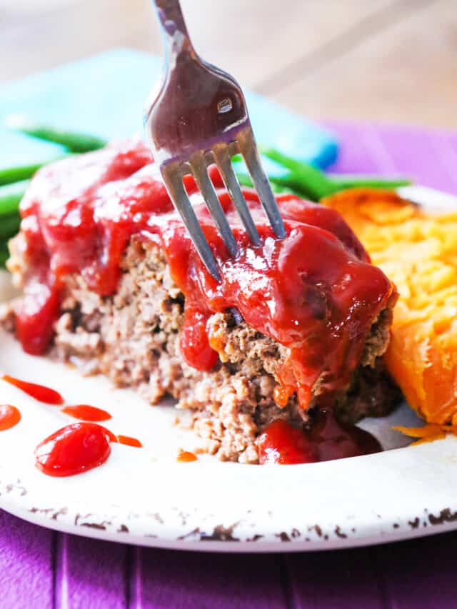 A fork stuck into the top of a slice of meatloaf topped with sauce. 