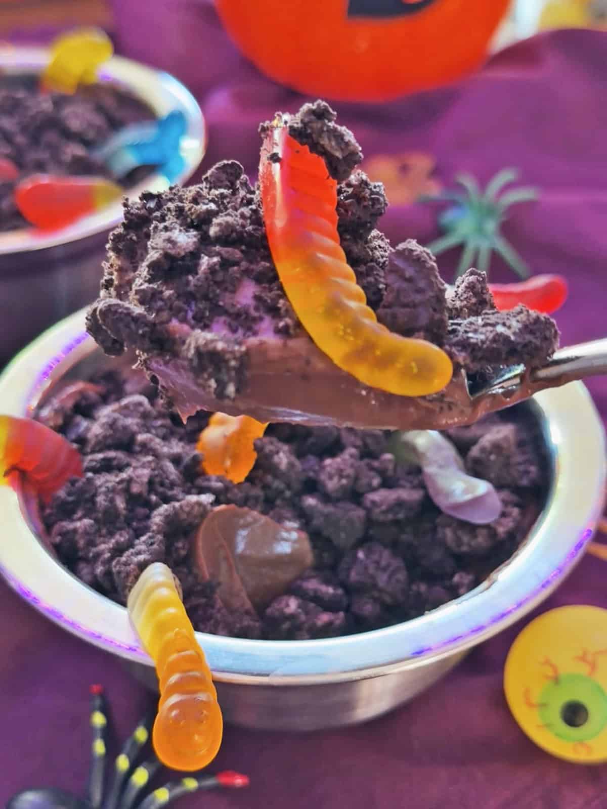 Chocolate pudding with gummy worms and Halloween decorations in the background.