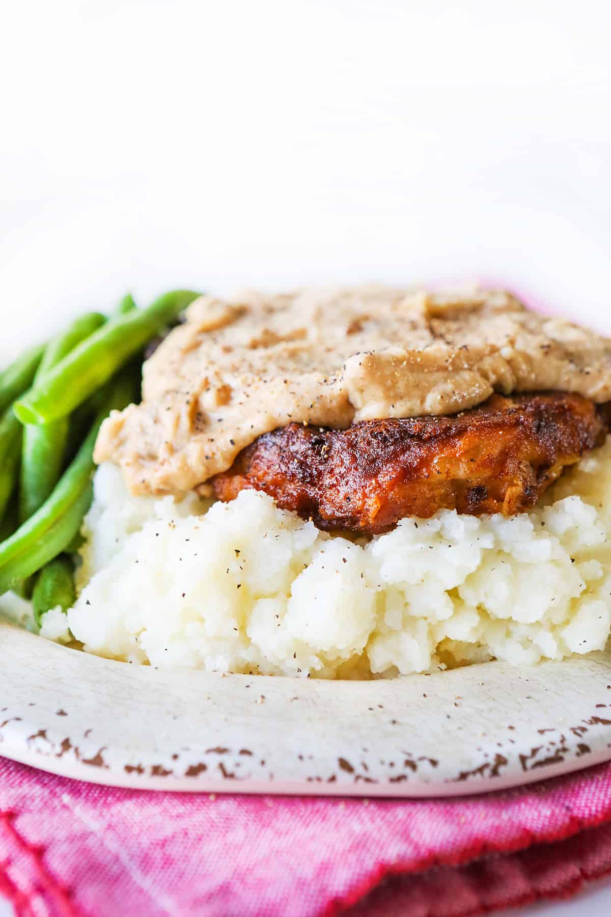 close up of a piece of chicken fried steak covered with thick gravy and sitting on top of mashed potatoes