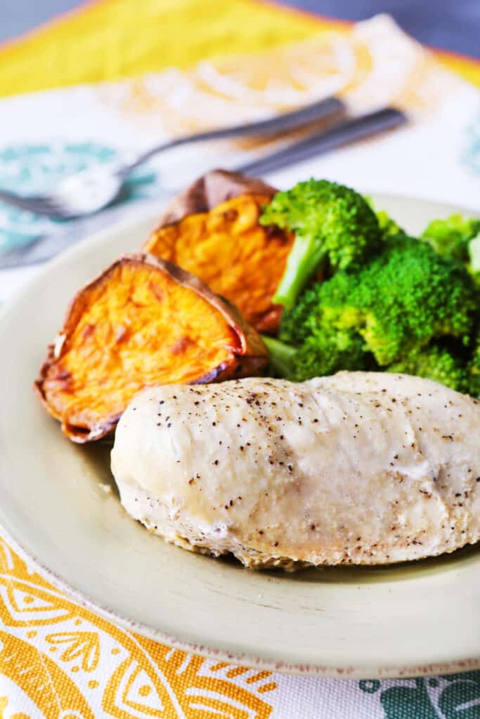 Grilled chicken on a plate with two halves of a sweet potato and broccoli alongside it. 