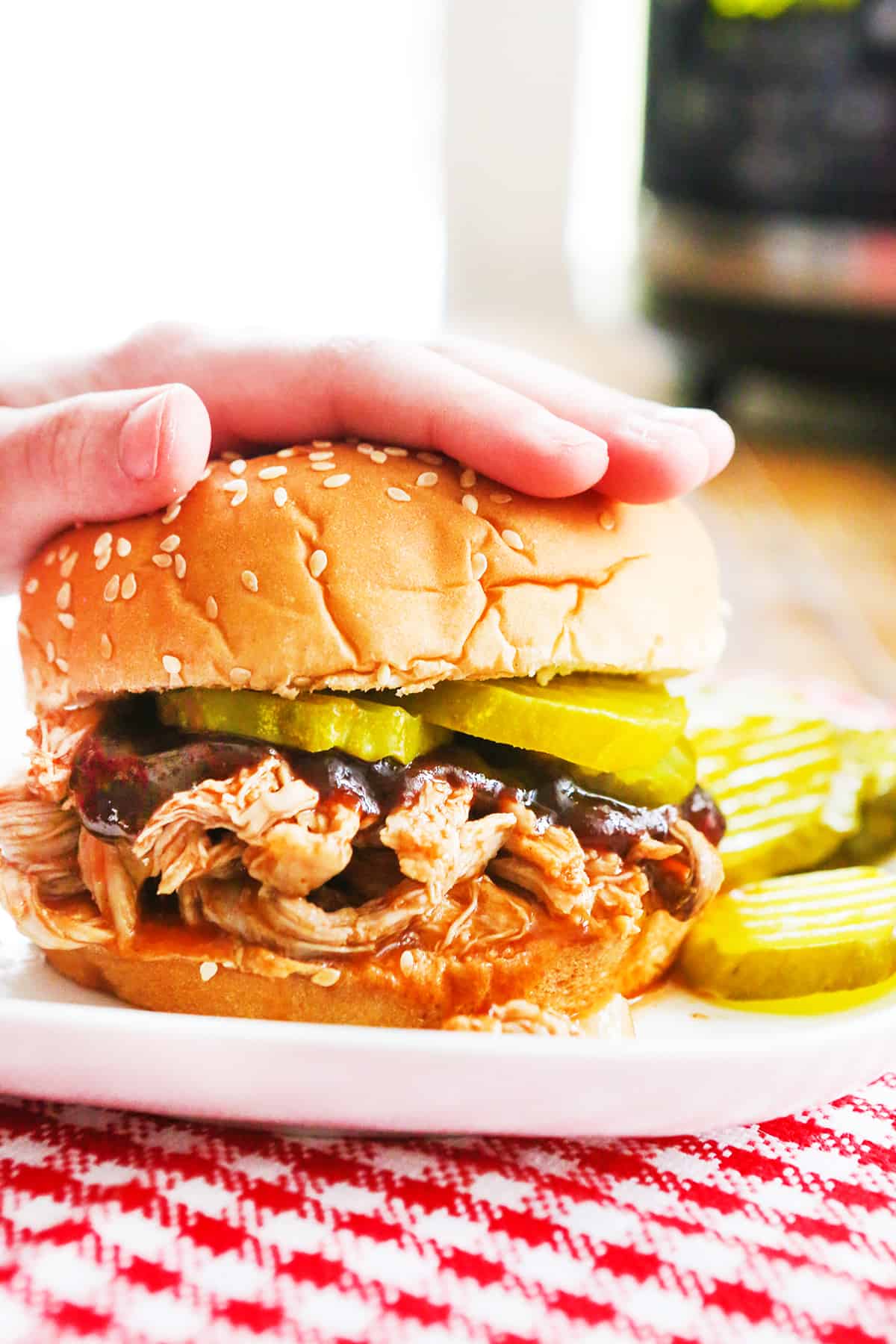 hand pressing down on the top bun of a pulled pork sandwich.