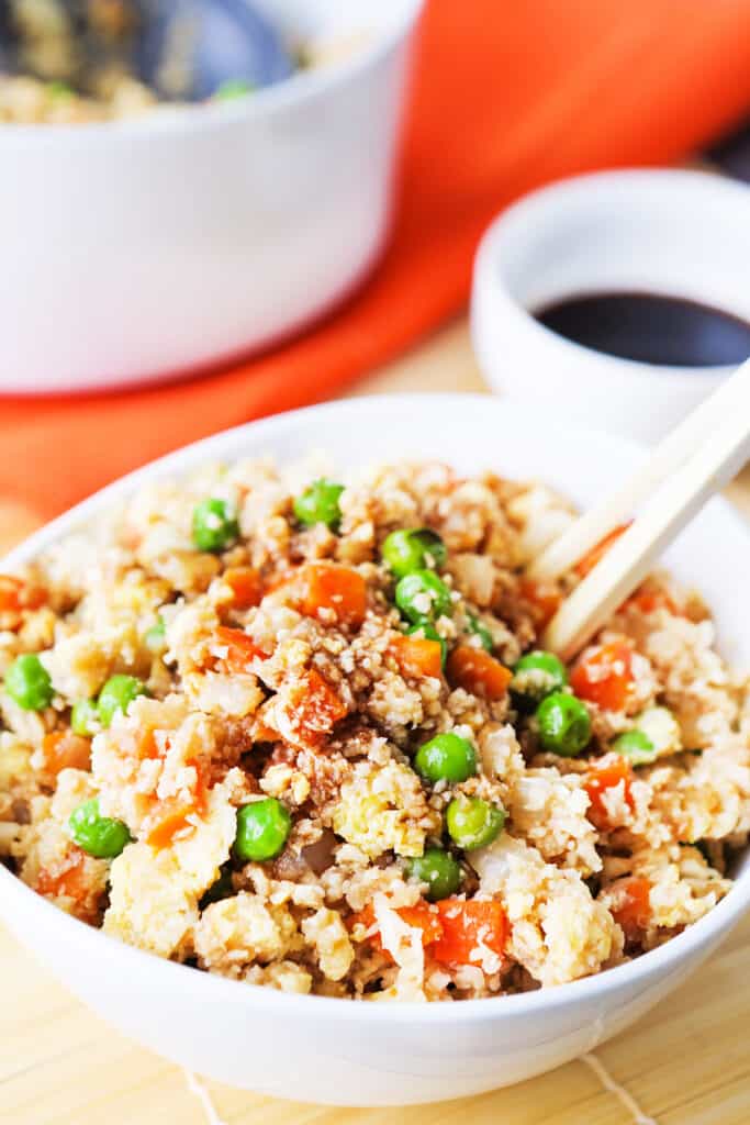 Bowl of cauliflower fried rice with chopsticks tucked into the dish. 