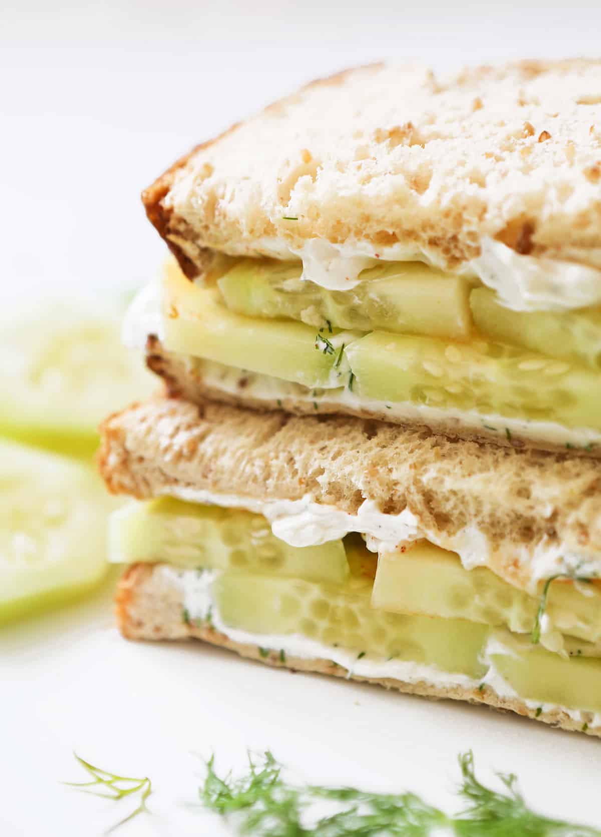 Cucumber cream cheese sandwich halves stacked on top of each other.