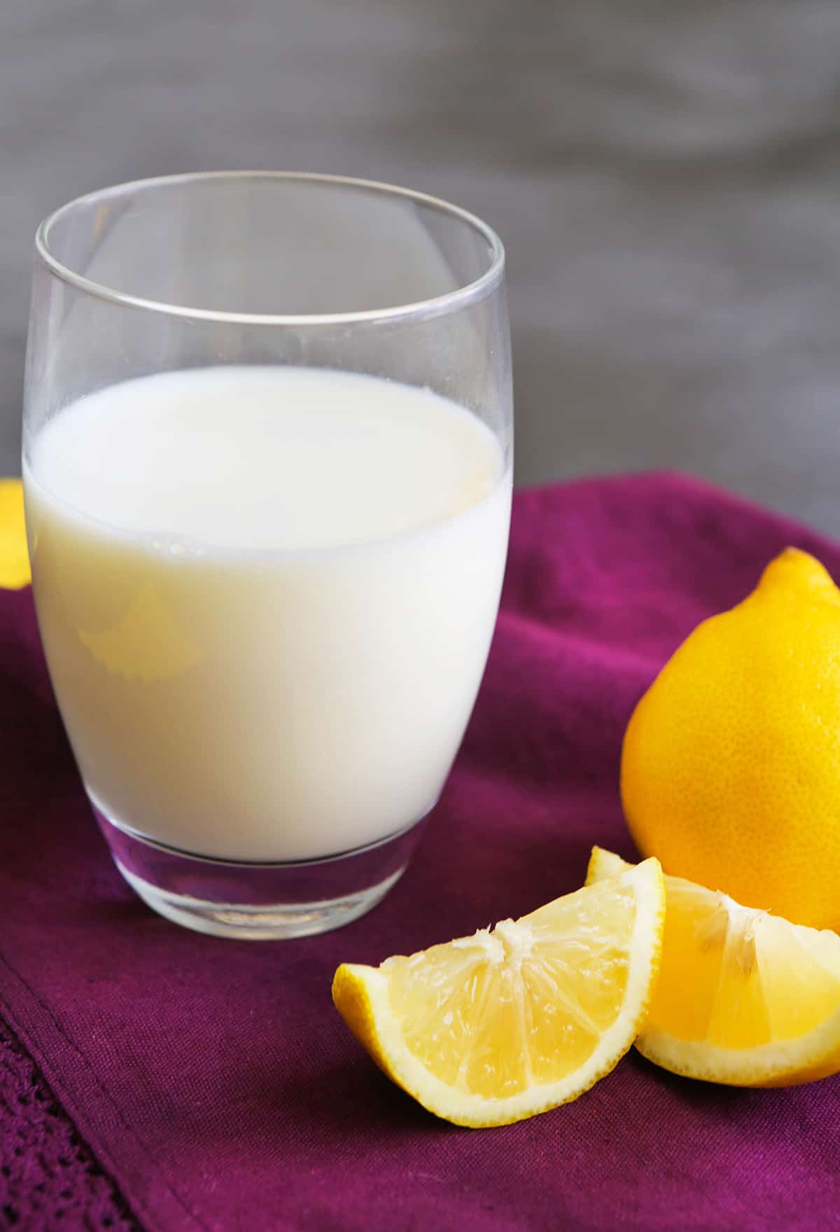 A glass of buttermilk sitting next to a lemon and lemon slices.