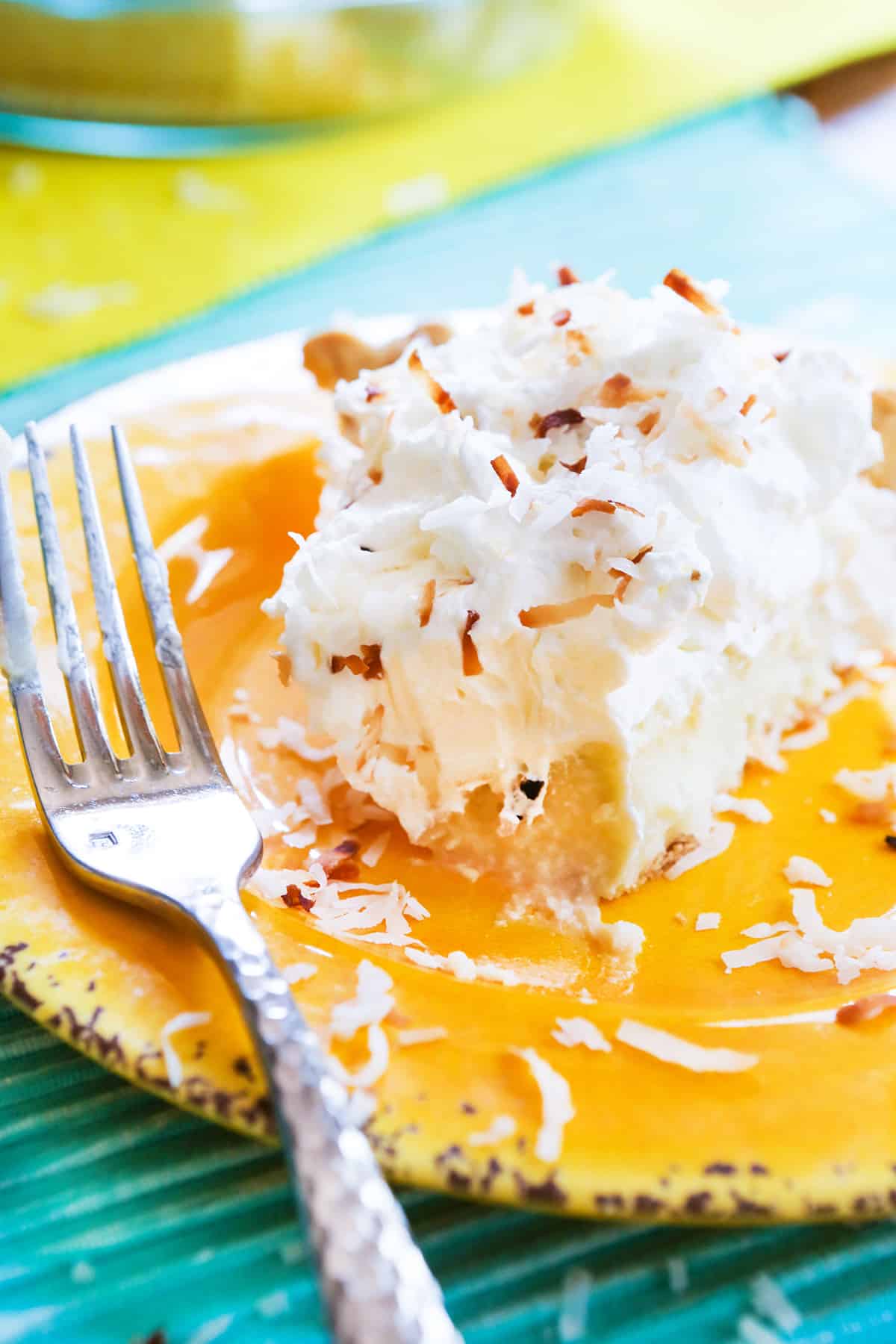 Slice of coconut cream pie on a plate with bite removed and fork nearby.