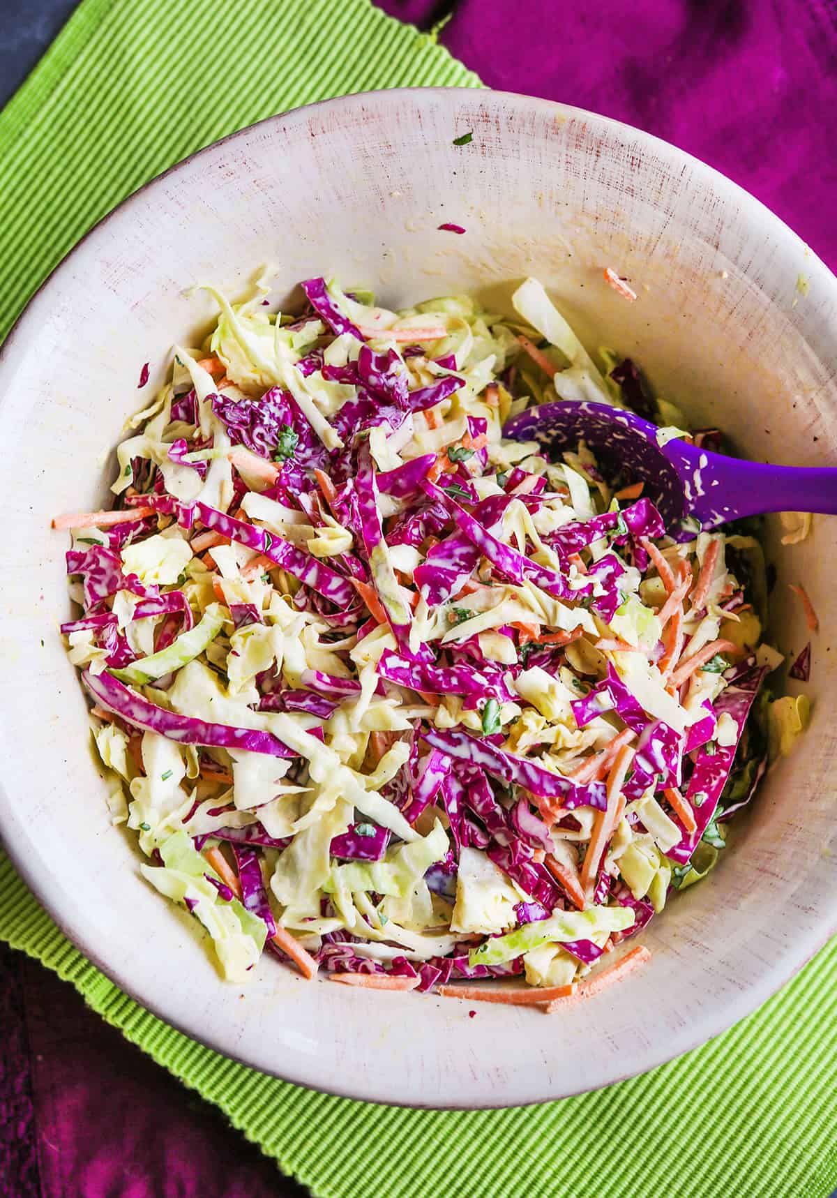 Coleslaw with apple cider vinegar in a mixing bowl with a purple spoon.