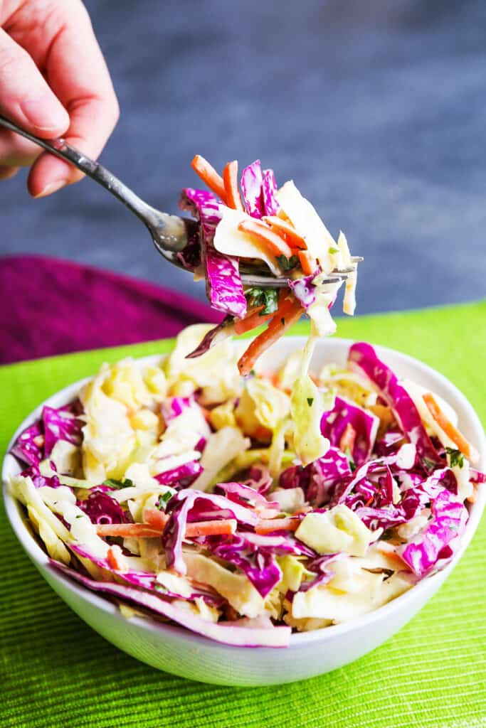 A fork full of coleslaw over a bowl. 