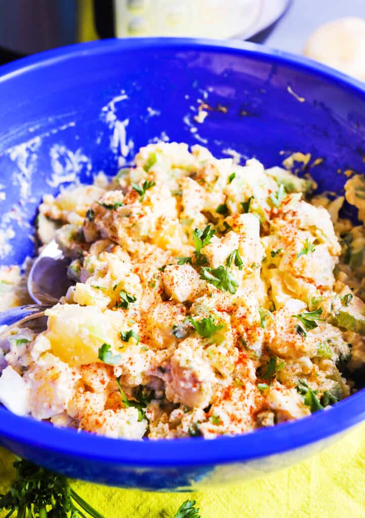 Potato salad with eggs in a serving bowl with a spoon tucked inside. 