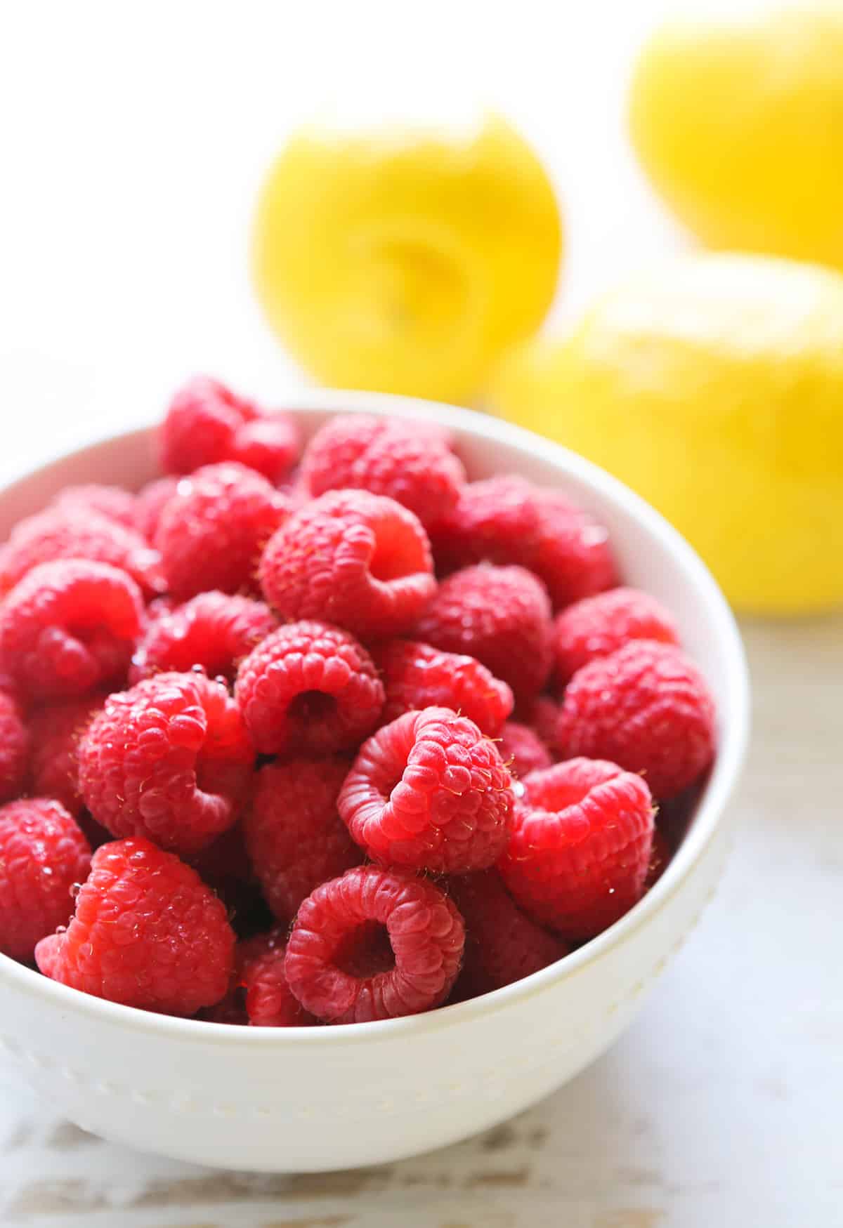 bowl of fresh raspberries sitting next to 3 lemons