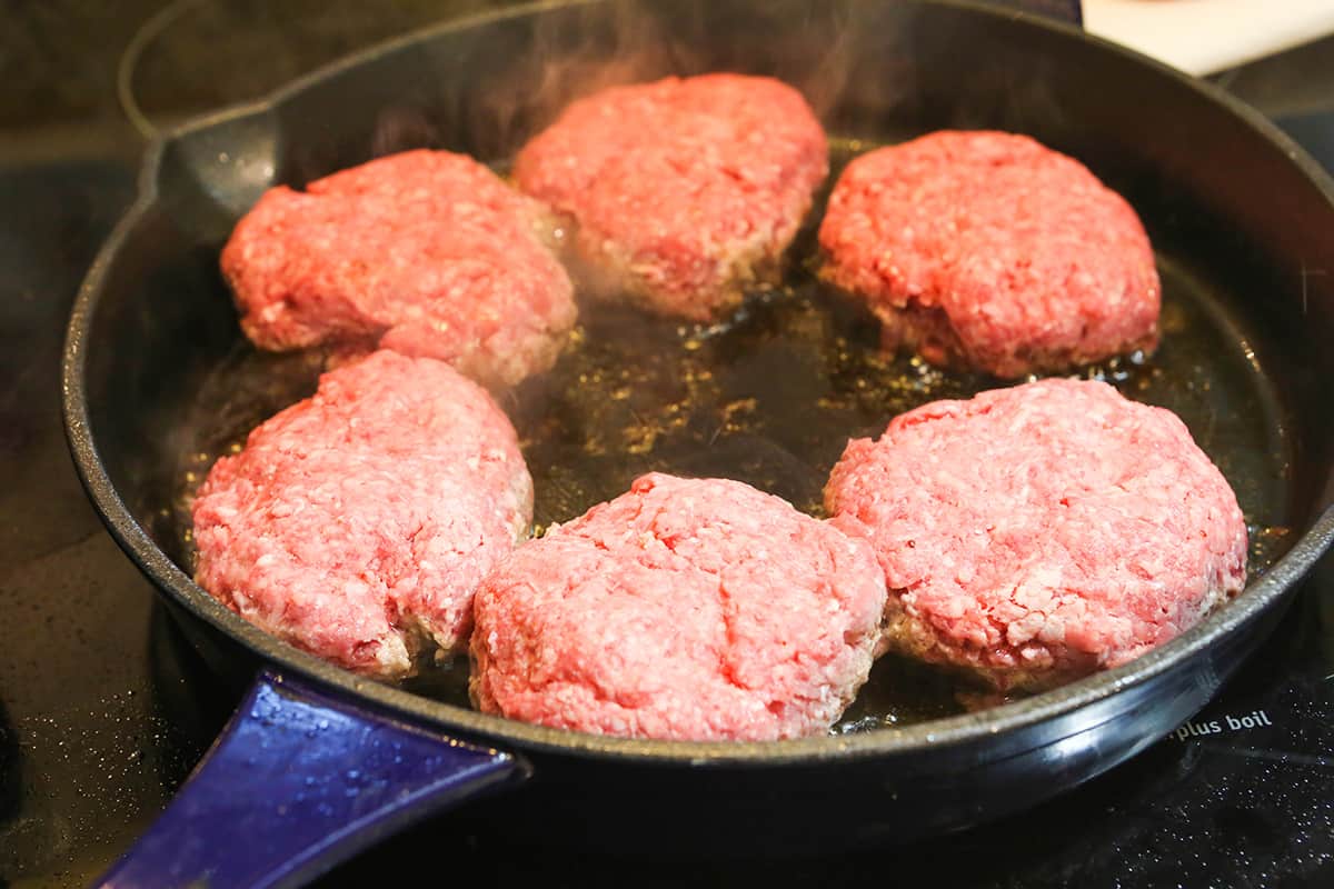 Burger patties in a skillet, cooking.