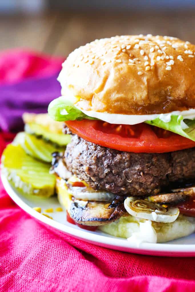 Five guys burger on a plate with pickles alongside it. 