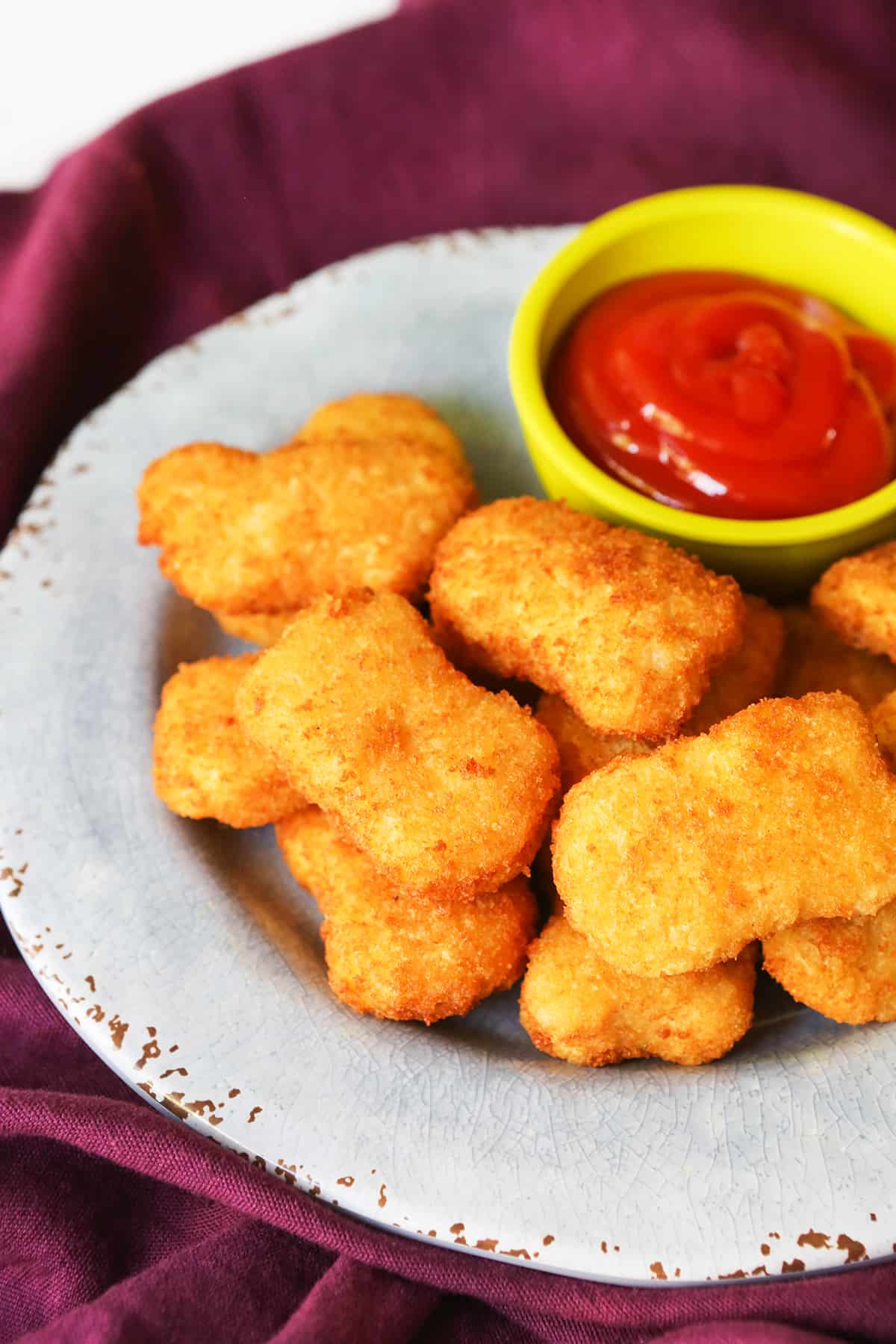 Plate stacked with air fryer chicken nuggets sitting next to a small bowl of ketchup.