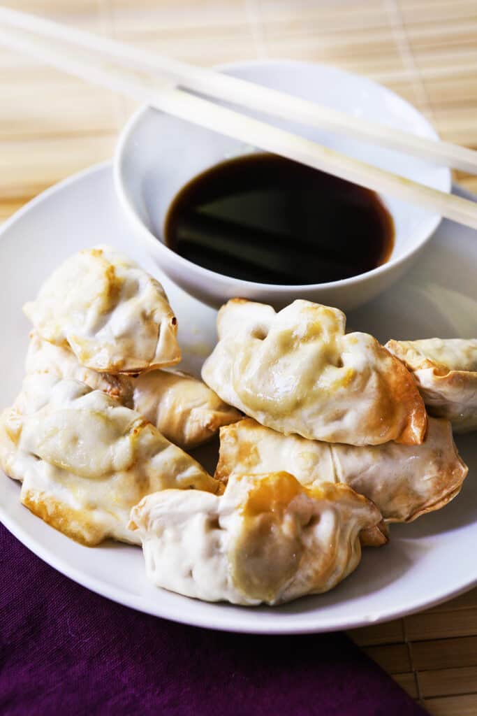 Plate of dumplings next to a small dish of soy sauce and some chopsticks. 