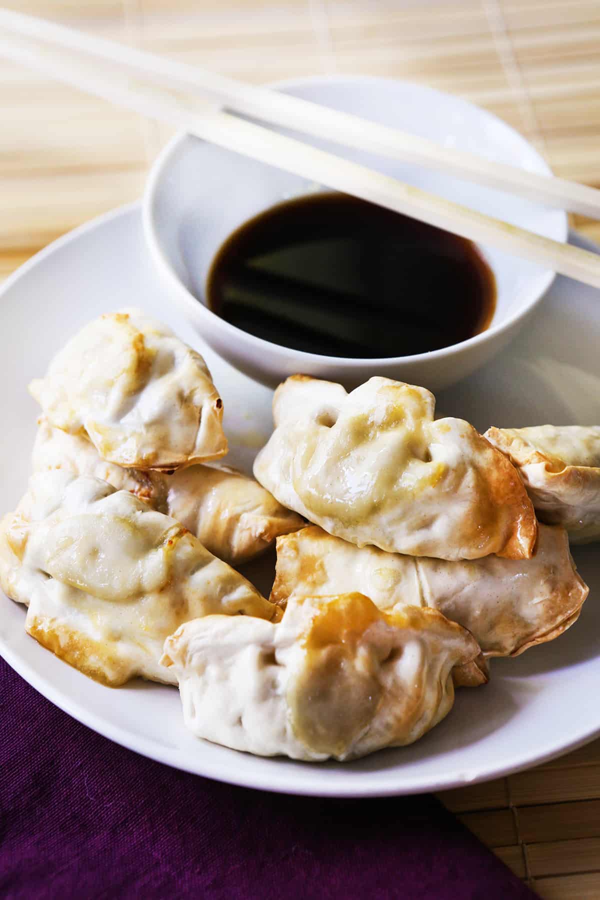 Chopsticks laying across a bowl of soy sauce, sitting next to a plate of dumplings.