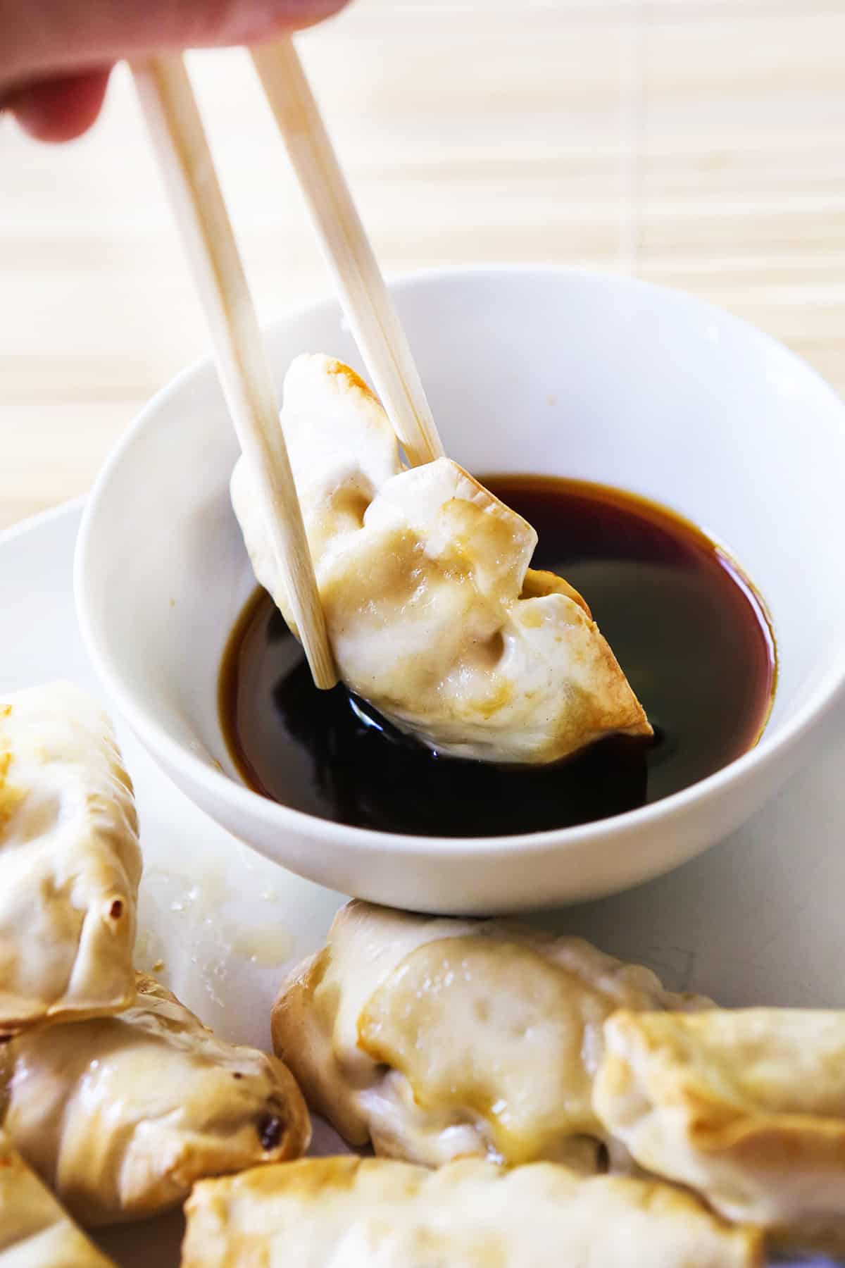 Chopsticks dipping a potsticker into a small bowl of soy sauce.